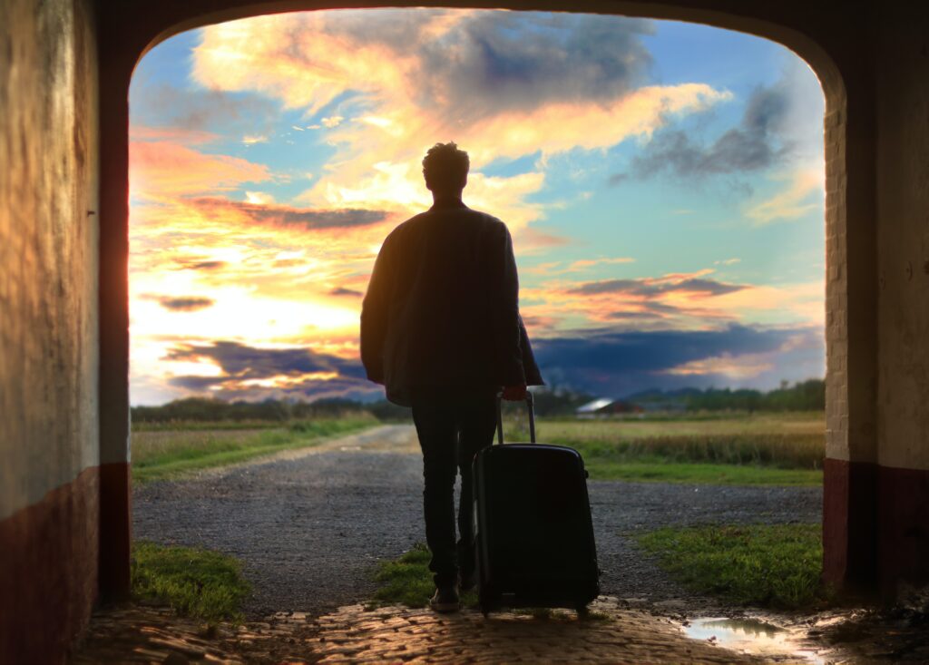 Man walking through tunnel with suitcase in front of sunset and blue skies