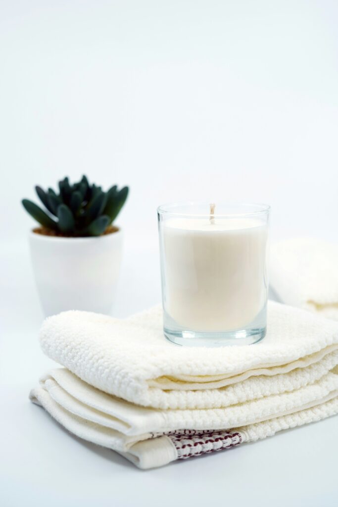 White candle on top of white cloth with small cactus in background in front of white backdrop