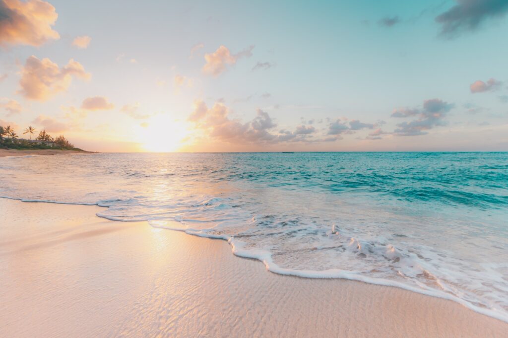 Sunset on sandy beach with clear blue waters and palm trees in the distance