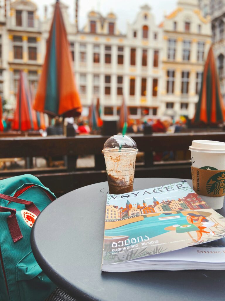 Coffee table with starbucks drinks, magazine and green backpack next to it in front of street background