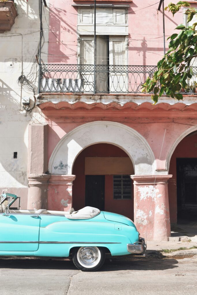 light blue cuban cadillac parked outside a pink building